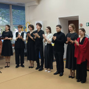 Студенты 3 курса НГТИ стоят в один ряд, они одеты в черную одежду, некоторые их них аплодируют. Слева стоит пара ведущих, перед ними стоит микрофон на стойке. 